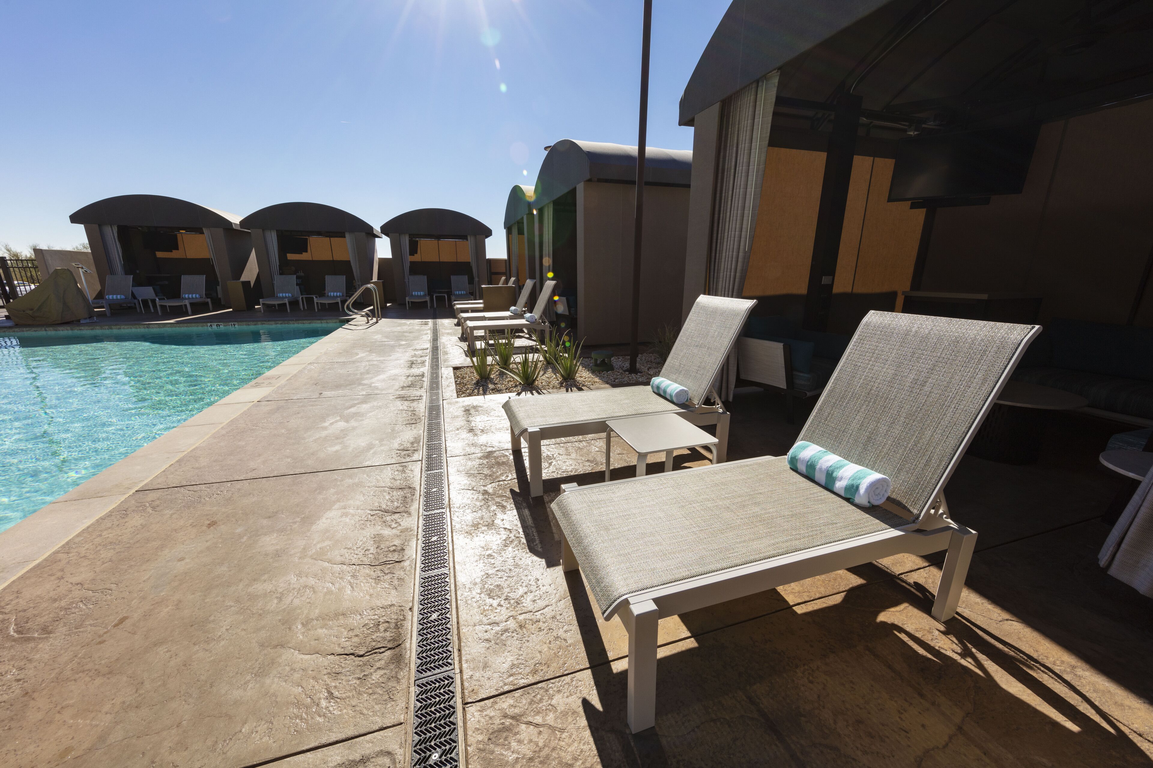Un espace aménagé au bord de la piscine, comprenant des chaises longues, une piscine et un coin salon abrité.