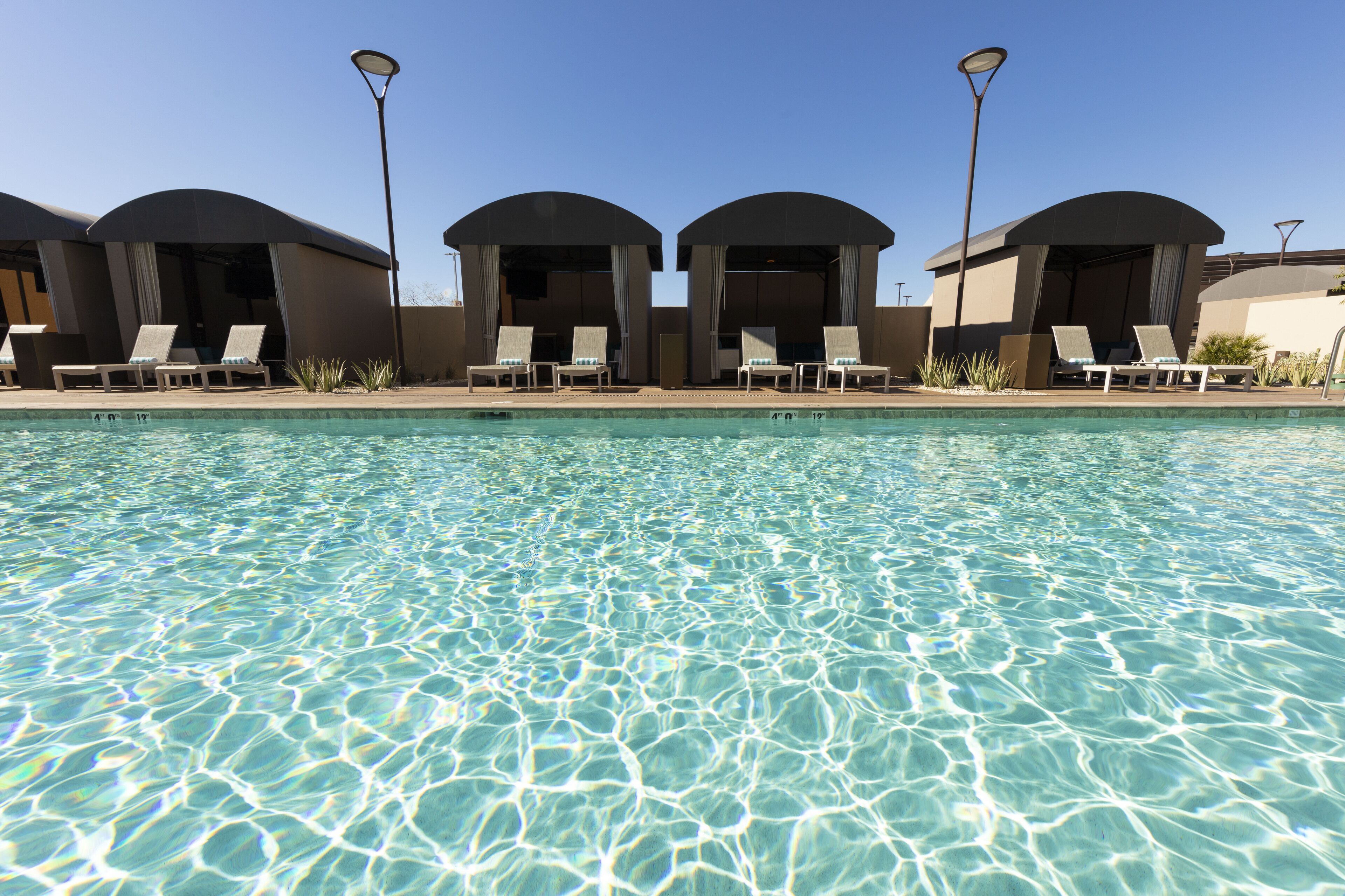 A pool with clear water and lounge chairs under shaded structures.