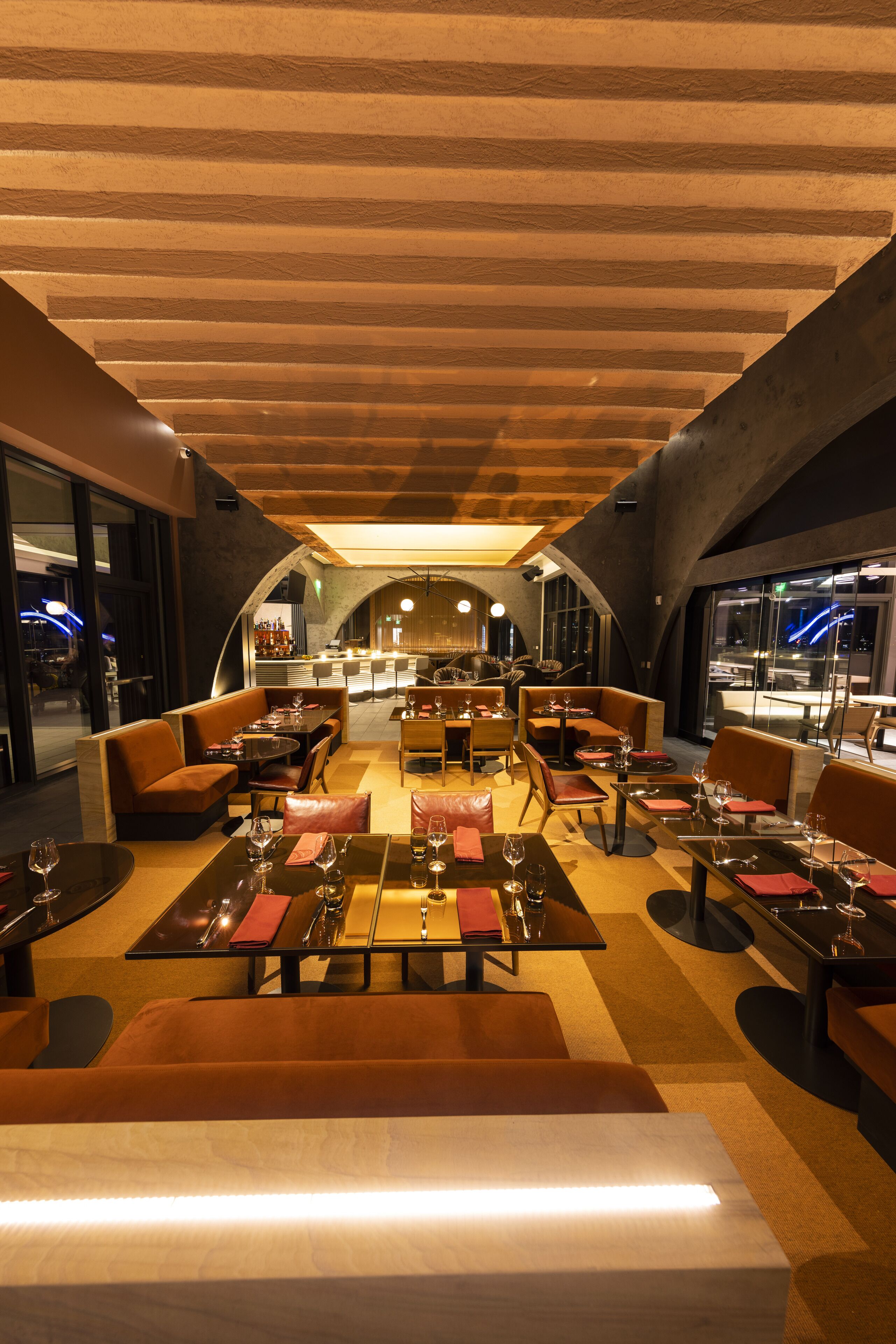 An indoor dining area with tables set for meals, cushioned seating, and a bar in the background.