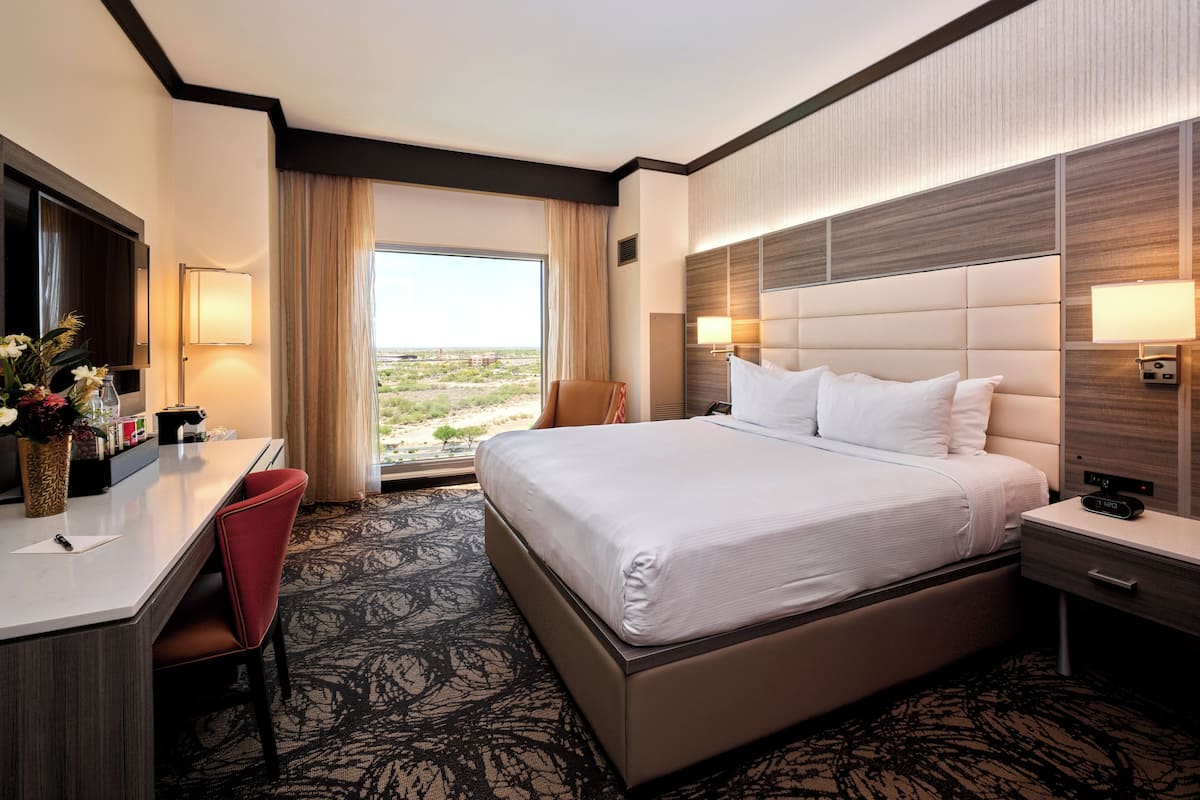 Habitación de hotel con una cama grande, un escritorio, una silla, un televisor y una ventana con vista al desierto.