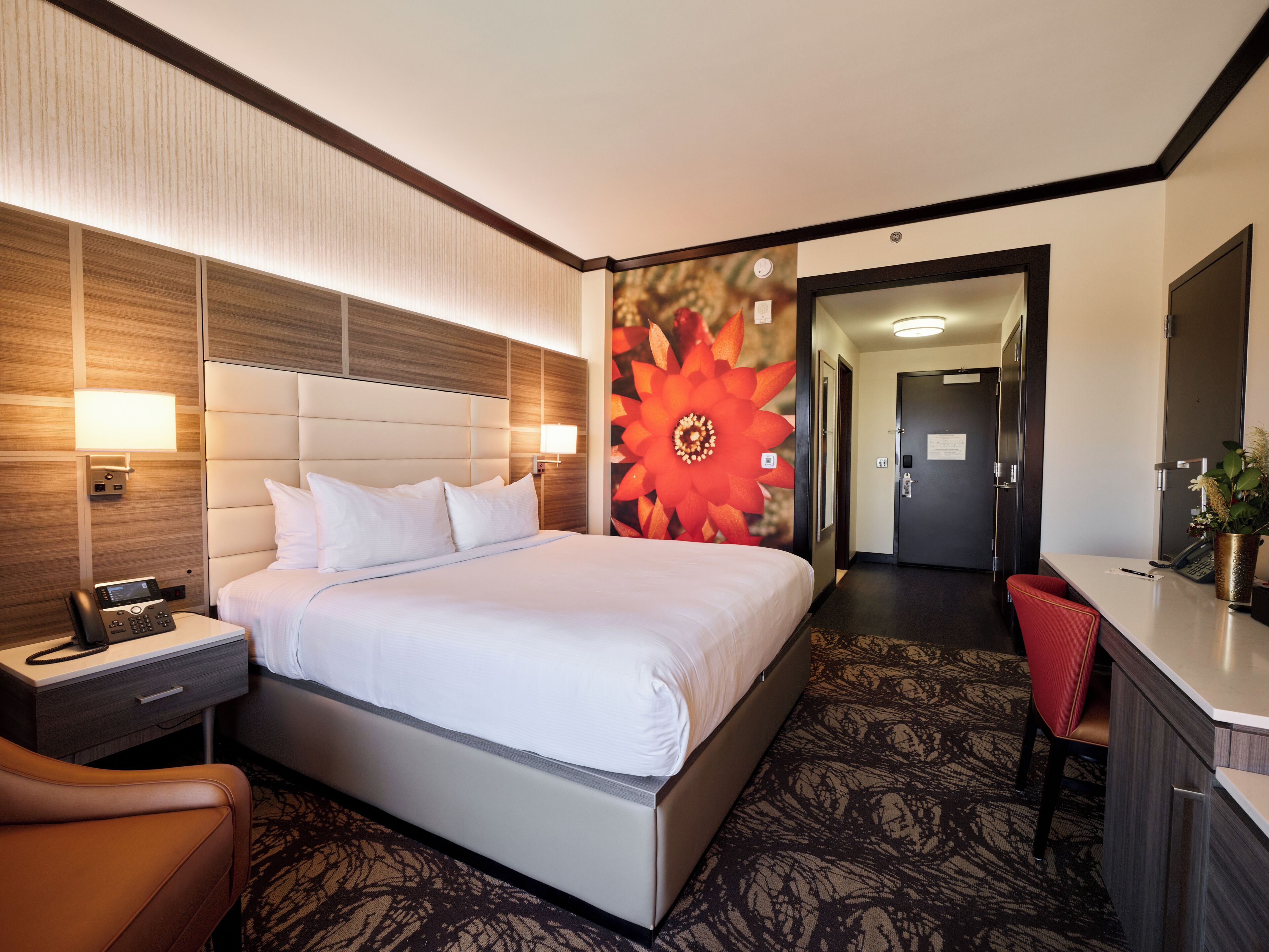 A hotel room with a bed, bedside table, lamp, and a desk with a chair.
