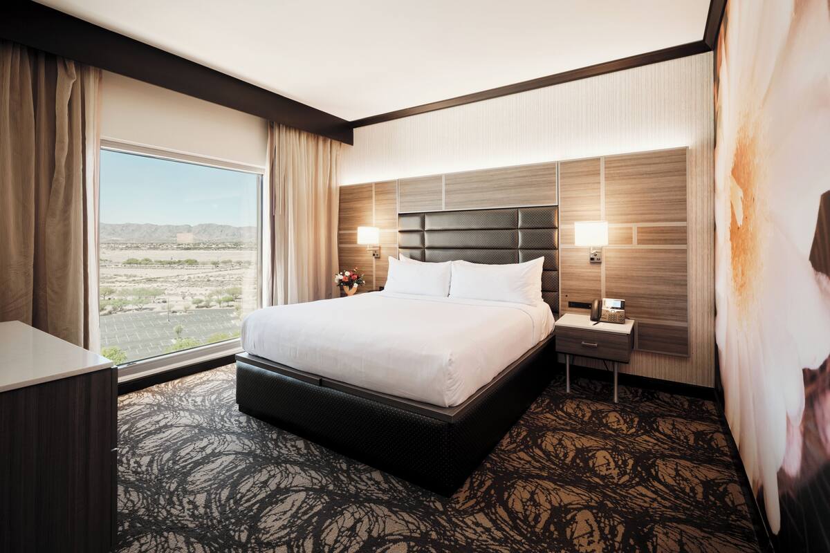 Habitación de hotel con una cama grande, una mesita de noche, un escritorio y vistas al desierto, además de un ventanal amplio.