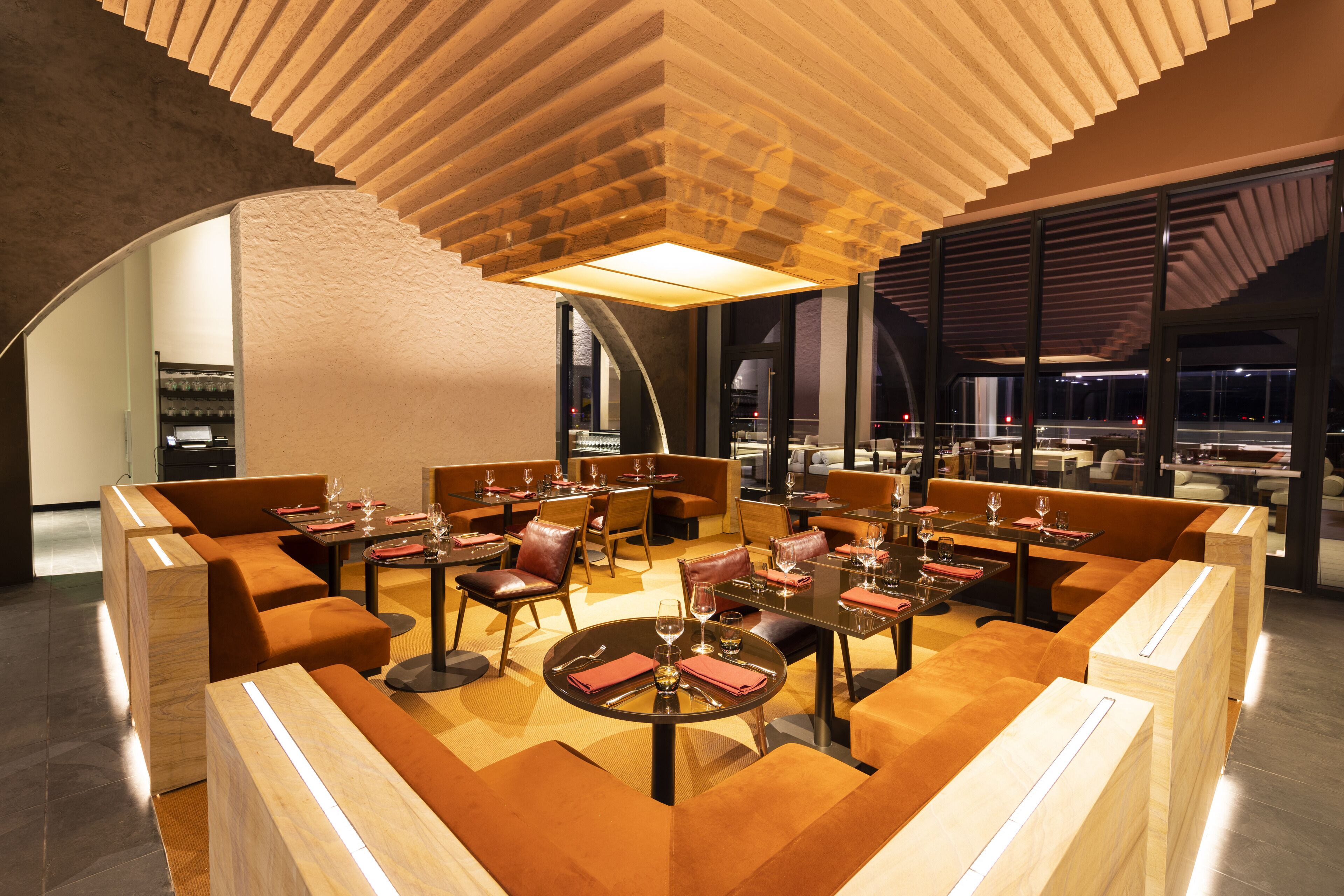 Un restaurante moderno con detalles de madera, mesas redondas y asientos de cuero.