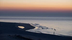 A beach with a flag on the sand, a person standing, and a calm sea. - Palm Beach Resort Orange Beach a Ramada by Wyndham (Orange Beach)