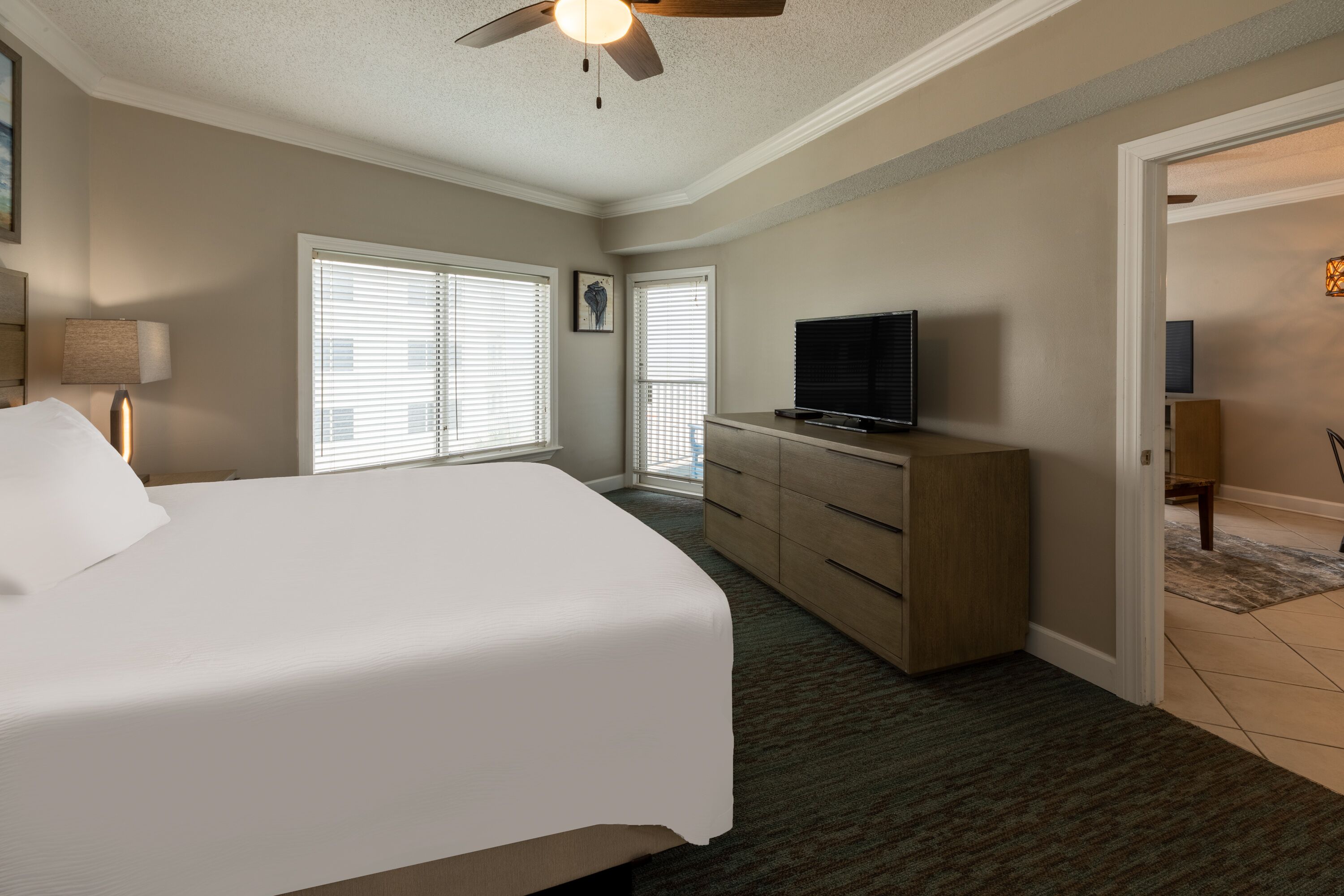 Ein Hotelzimmer mit einem großen Bett, einem Schminktisch, einem Fernseher und einem Deckenventilator.
