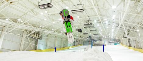 Una amplia instalación interior para practicar snowboard, con techo alto y vigas estructurales visibles.