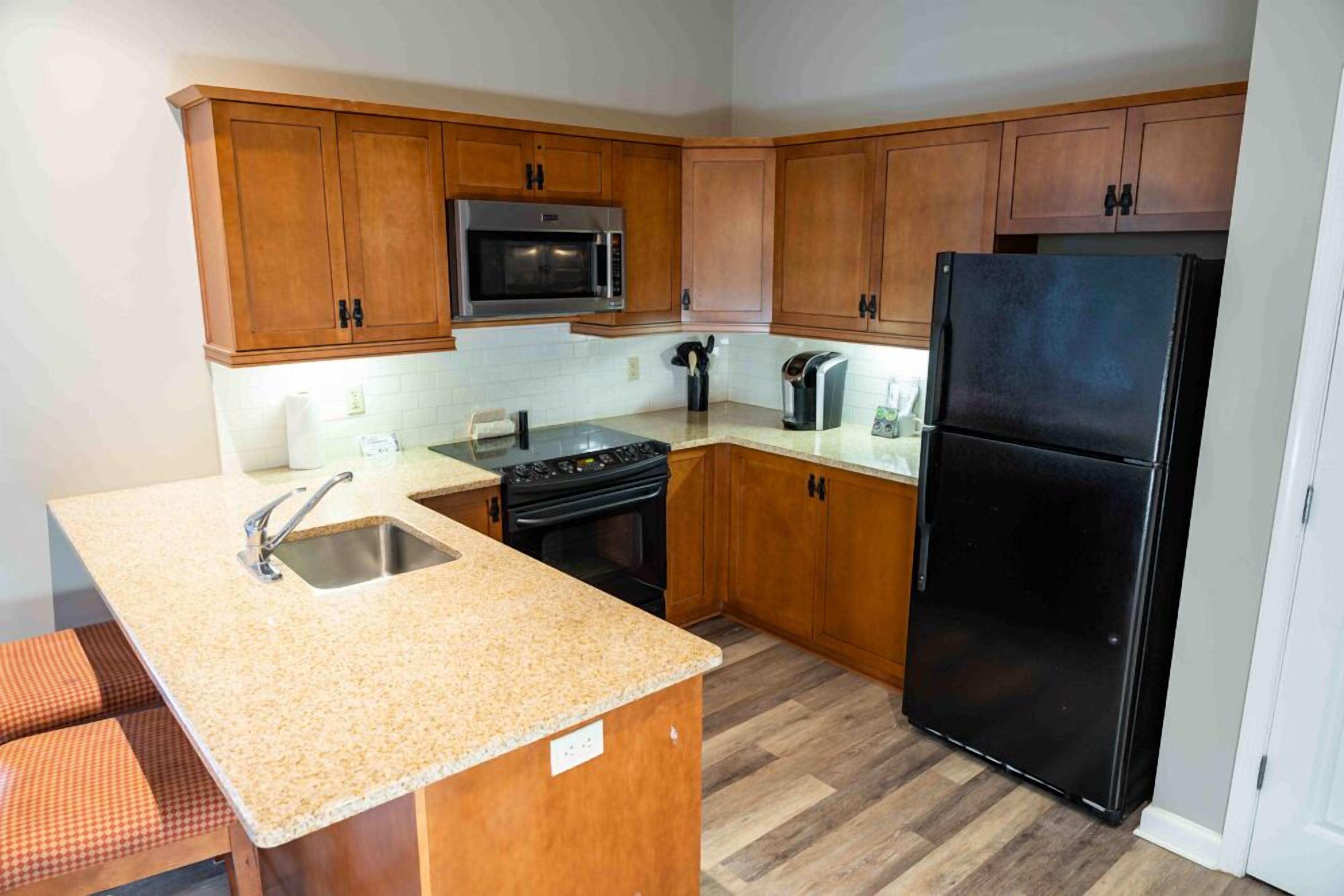 A kitchen with wooden cabinets, a stainless steel sink, a black refrigerator, a microwave, and a stove.