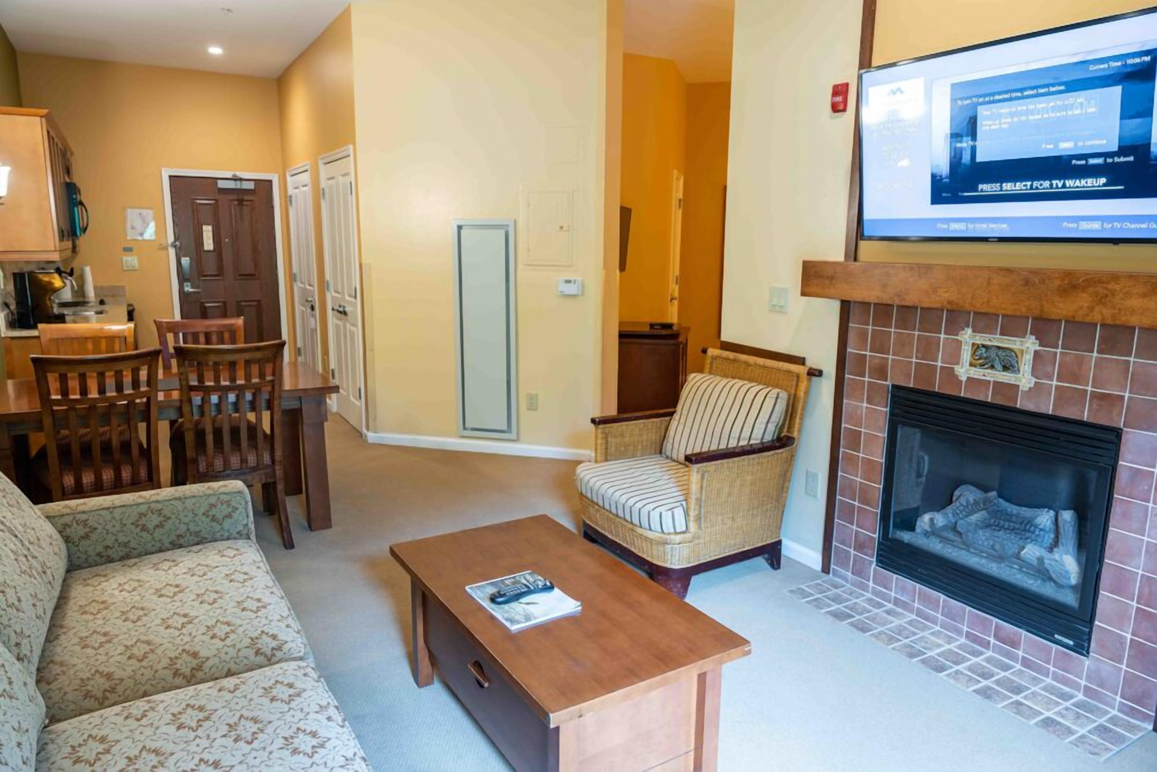 A living room with a sofa, a coffee table, a fireplace, a television, and a dining area with chairs and a table.