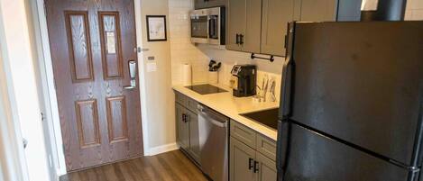 Una cocina con gabinetes grises, un refrigerador negro, un microondas y un lavavajillas.