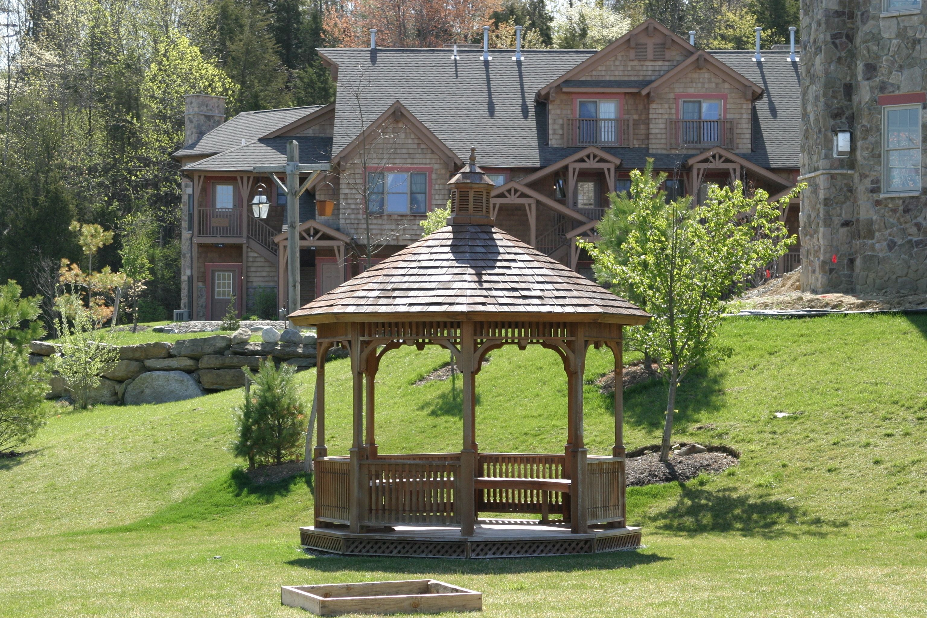 A gazebo in a landscaped area with a large stone building in the background.