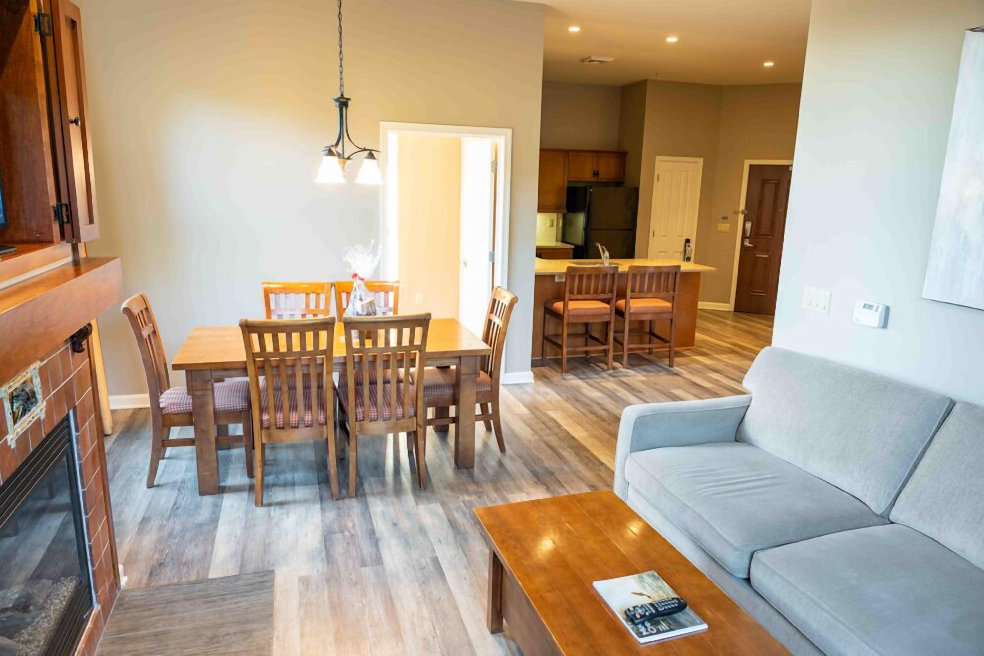 A modern living room with a sofa, a dining table with chairs, a fireplace, and a kitchen in the background.