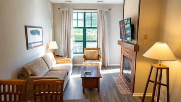 Een woonkamer met een bank, fauteuils, een salontafel, een open haard en een aan de muur bevestigde televisie.