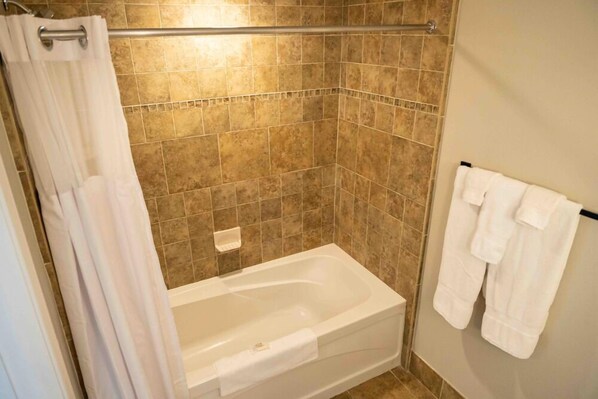A bathroom with a bathtub, tiled walls, a shower curtain, and a towel rack with towels. - Mountain Creek (Vernon)