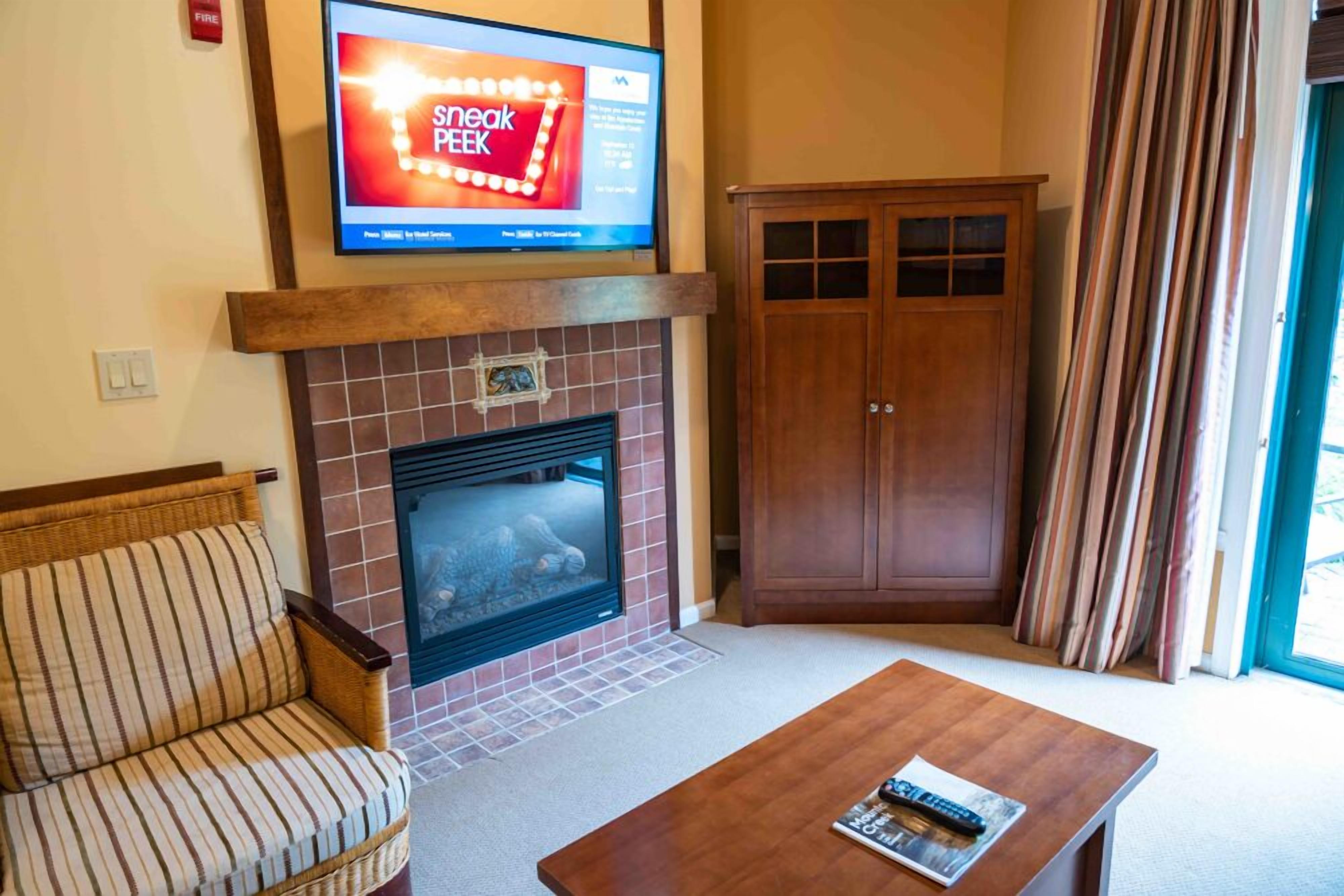 A living room with a fireplace, a sofa, a coffee table, and a television mounted above the fireplace.