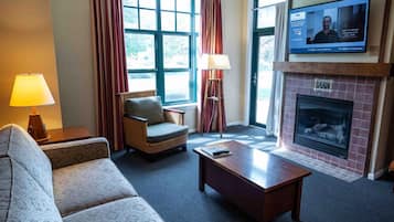 A hotel room with a sofa, armchair, coffee table, fireplace, TV, and curtains.