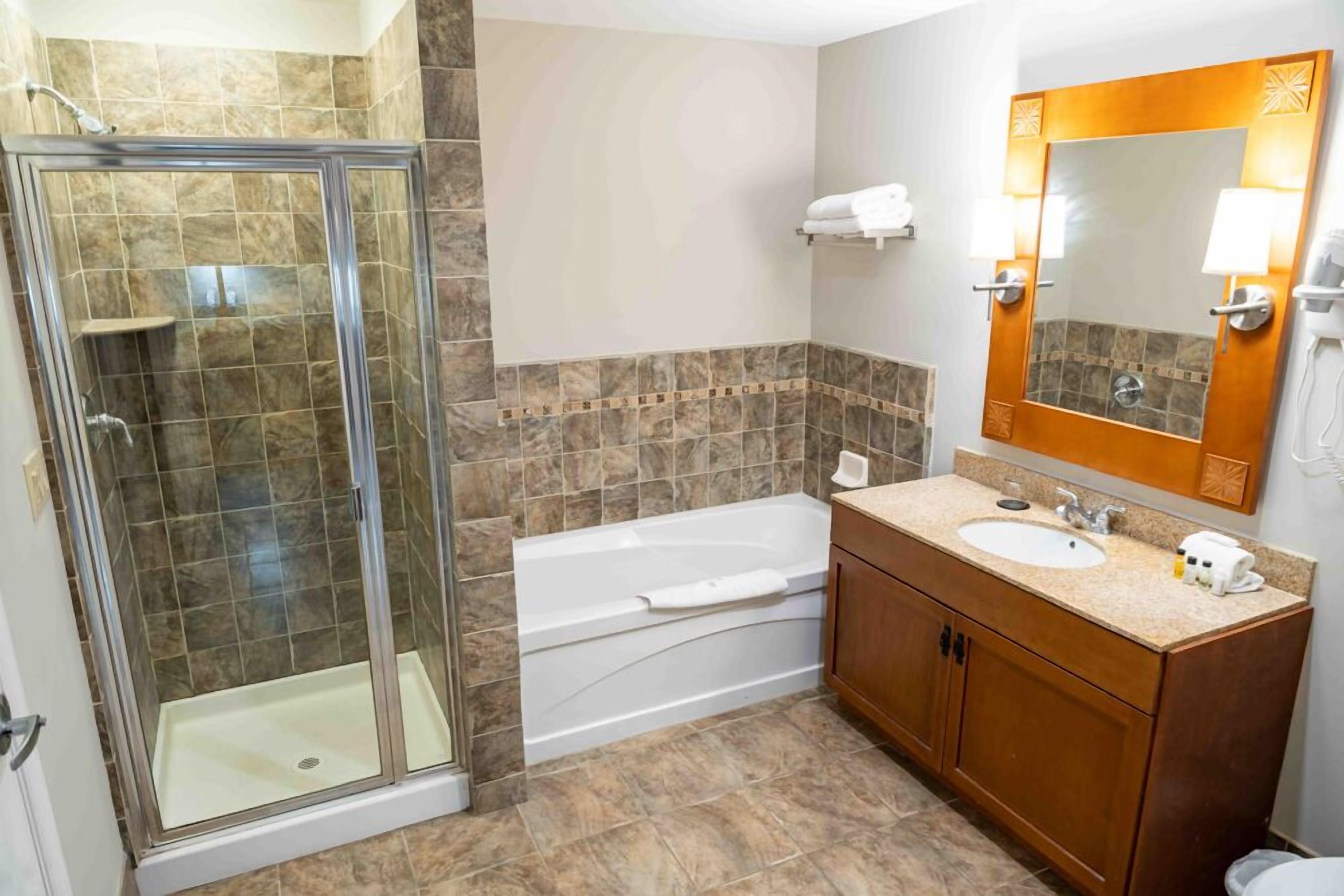 A bathroom with a glass-enclosed shower, a bathtub, a sink with a vanity, and a mirror with wall sconces.