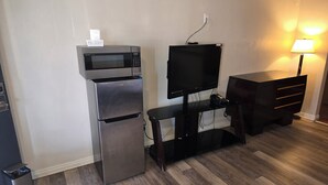 Eine kleine Küchenzeile mit Mikrowelle, Kühlschrank und einem Flachbildfernseher auf einem Standfuß.