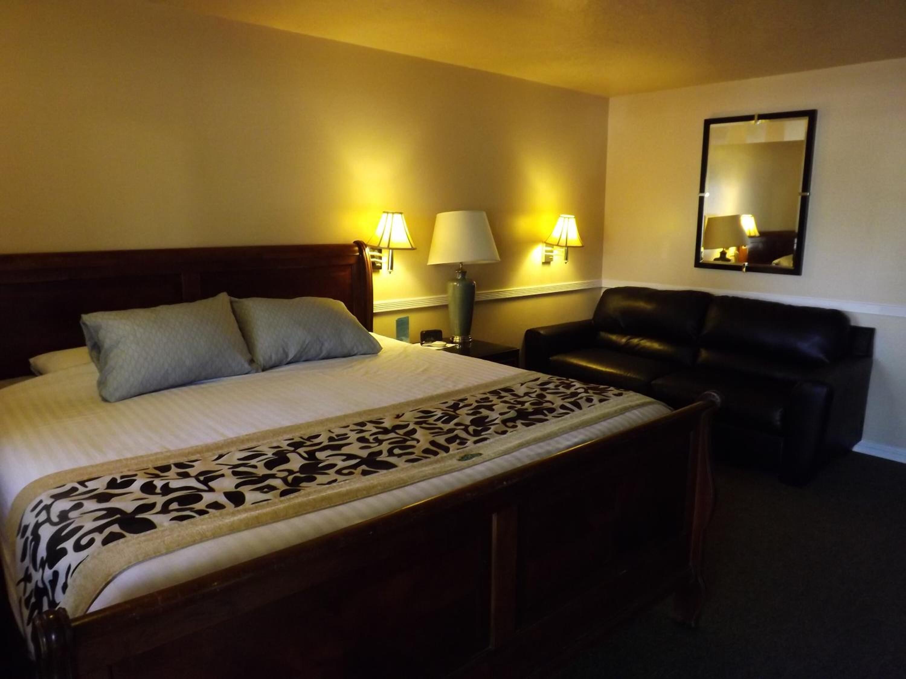 A hotel room with a bed, two bedside lamps, a black leather chair, and a mirror on the wall.