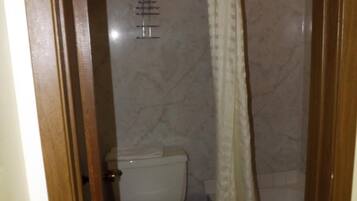 Un baño pequeño con inodoro, cortina de ducha y pared de mármol.