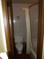Un baño pequeño con inodoro, cortina de ducha y pared de mármol.