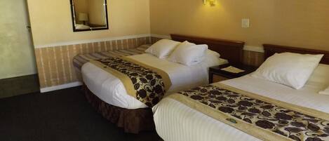 A hotel room with two beds, a mirror, a nightstand, and a wall-mounted lamp.