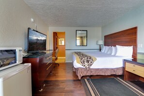Una habitación de hotel con cama, escritorio, televisión, microondas y refrigerador pequeño.