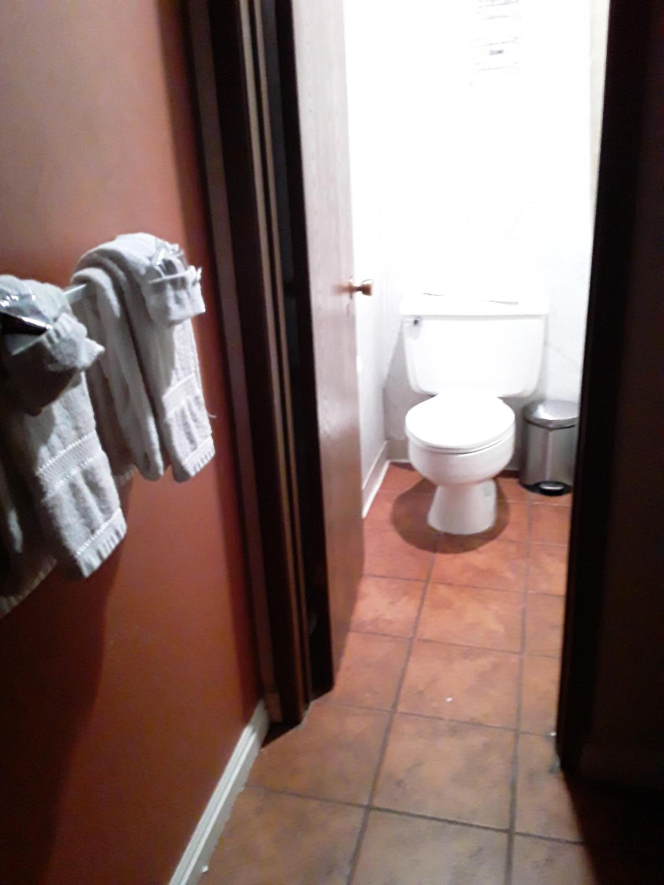 Un baño con inodoro, un cubo de basura y toallas colgadas en un perchero.