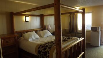 Un lit à baldaquin en bois, recouvert d’un plaid à motifs, avec une table de chevet, une lampe et une fenêtre avec des rideaux.