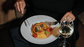Uma pessoa segurando um garfo e uma faca, com um prato de comida e um copo de água sobre a mesa.