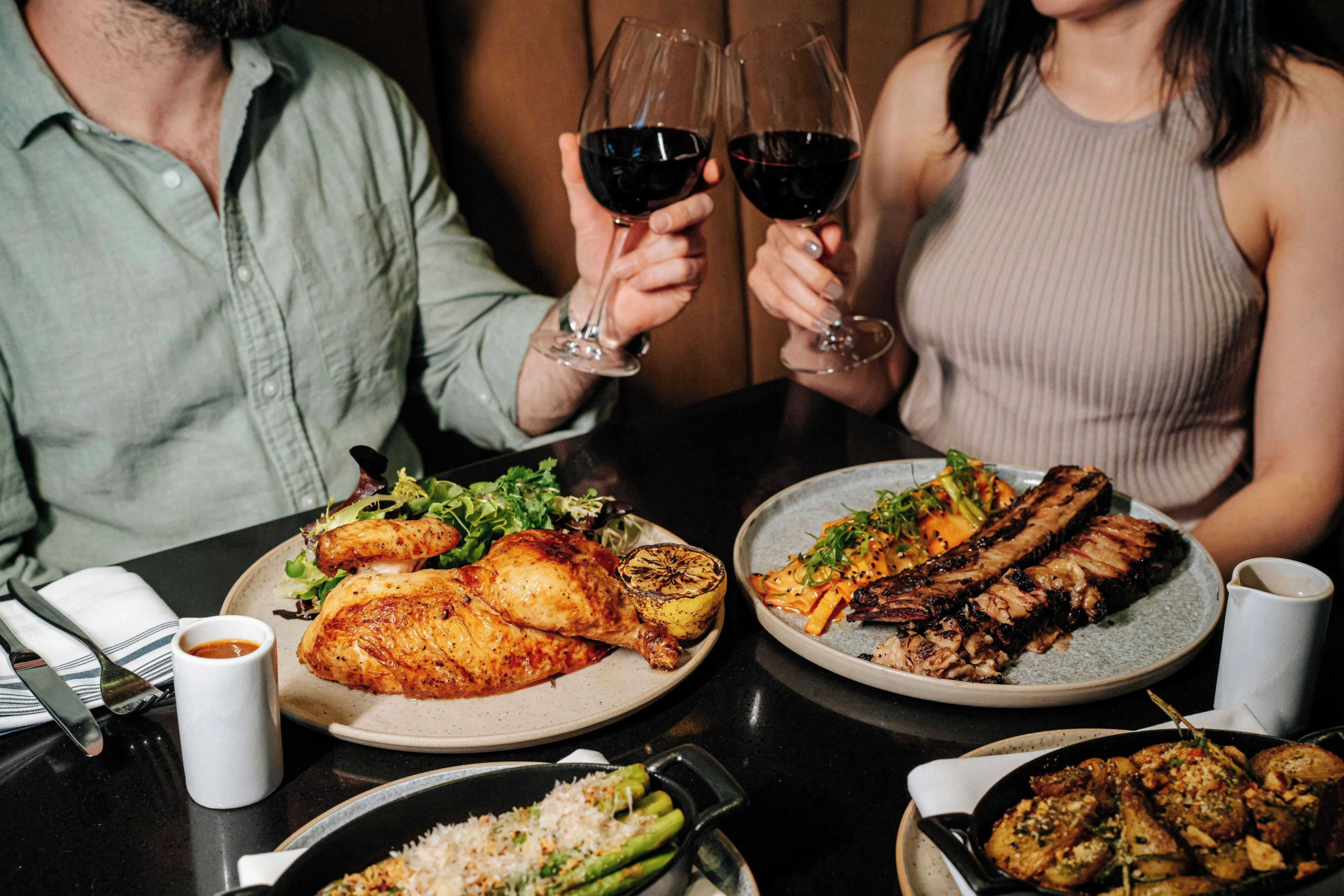 A dining table with plates of food, glasses of red wine, and a white mug.