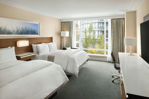 Een hotelkamer met twee bedden, een bureau, een televisie en een groot raam met gordijnen.