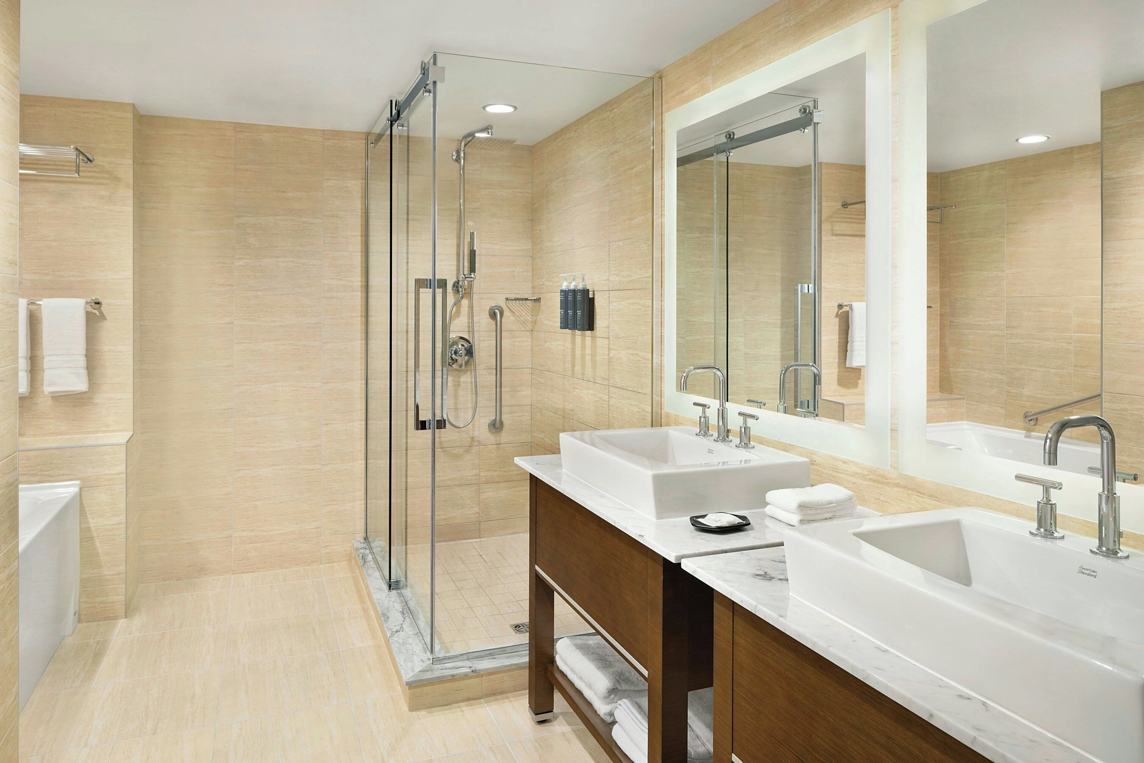A modern bathroom with two sinks, a large mirror, and a glass-enclosed shower.