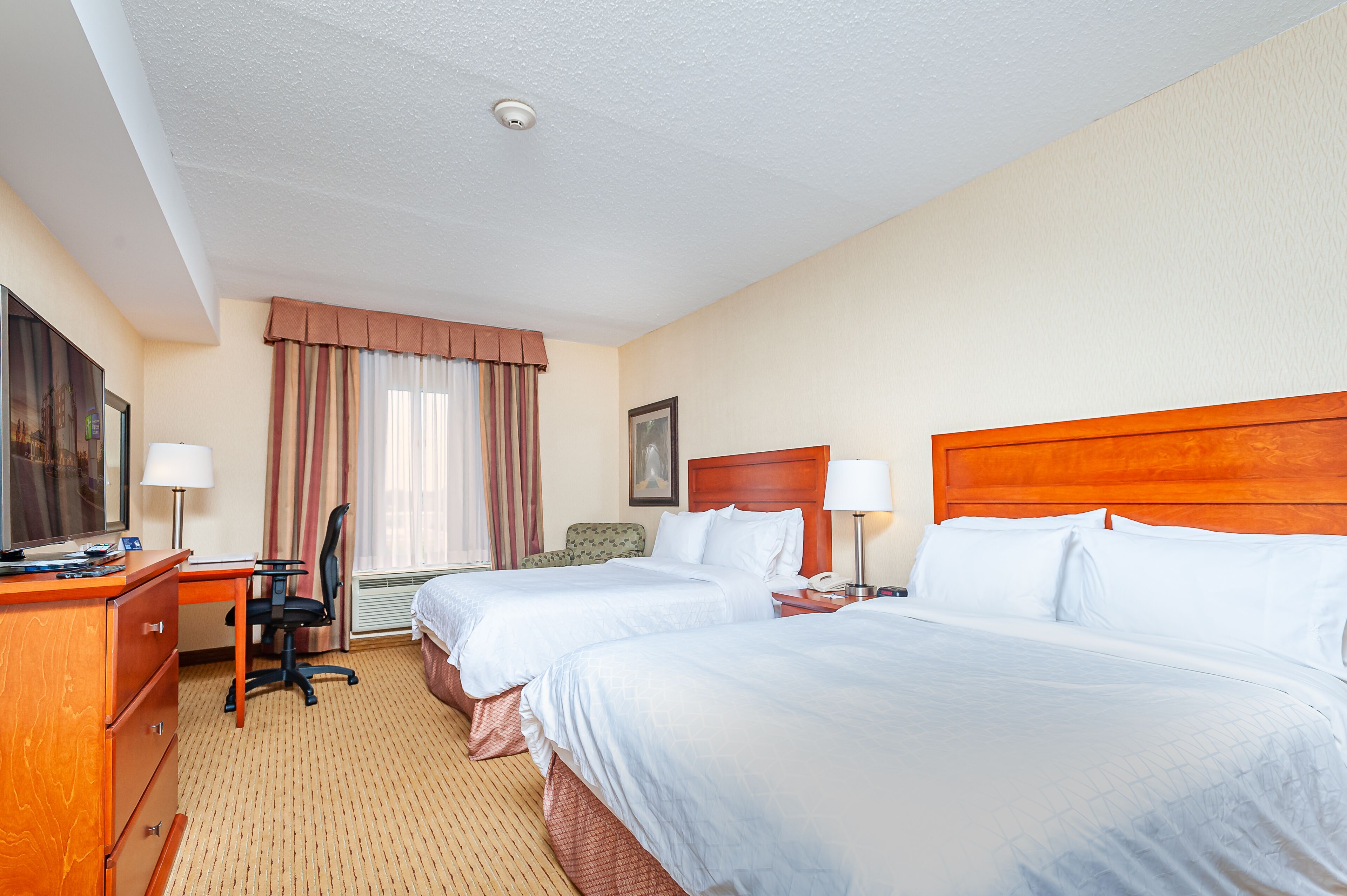 A hotel room with two beds, a desk with a chair, a television, and a window with curtains.