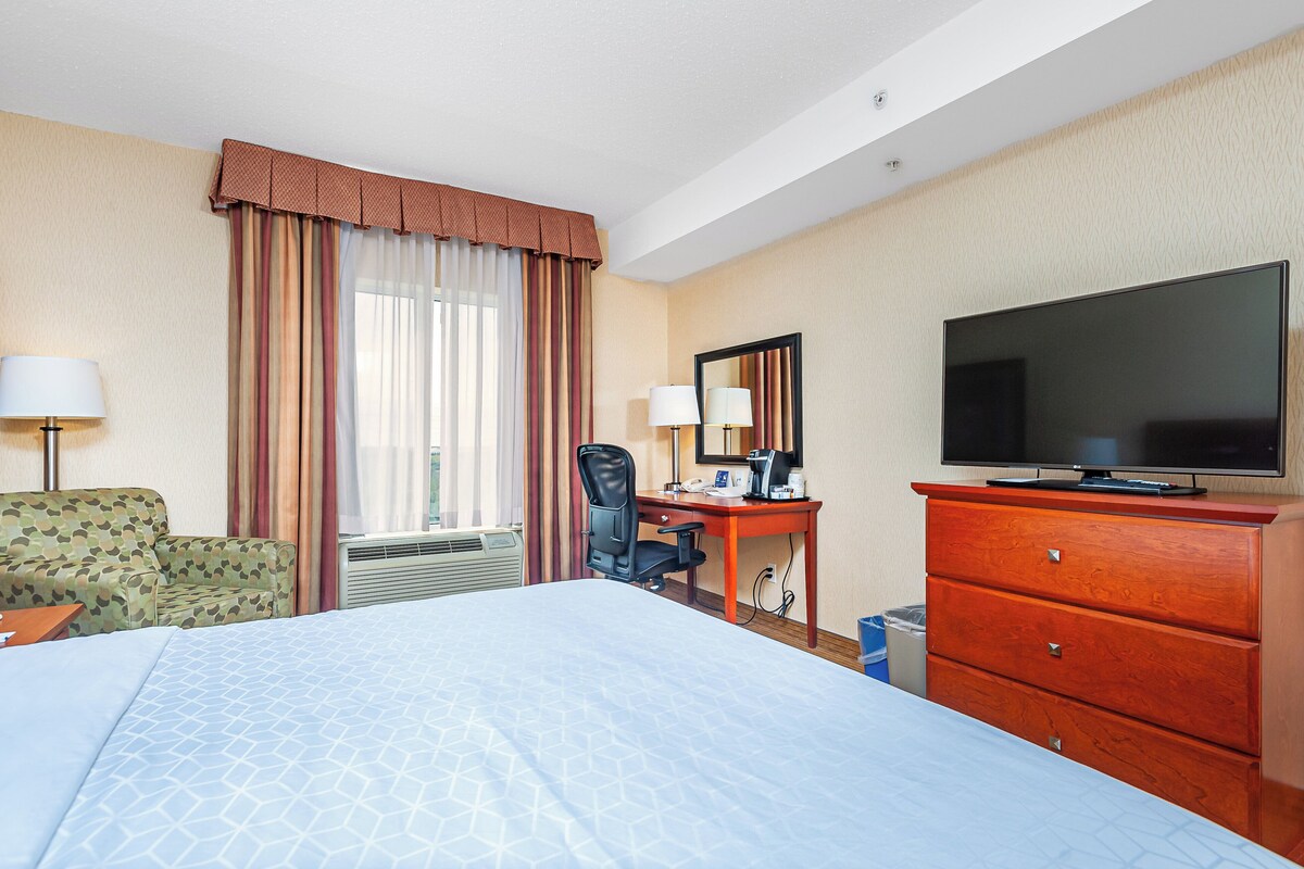 Habitación de hotel con cama, escritorio, silla, televisor y ventana con cortinas.