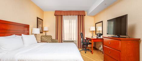 A hotel room with a large bed, a desk with a computer, a television, and a chair.