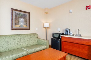 Una habitación de hotel con sofá, una mesa, una kitchenette con microondas, cafetera y lavabo.