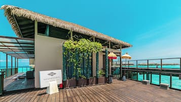 A wooden deck with a sign for Mandara Spa, a thatched roof structure, and a view of the ocean.