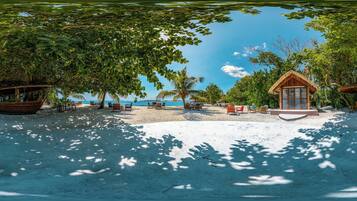 A beach with a wooden boat, lounge chairs, and a small building with a thatched roof.