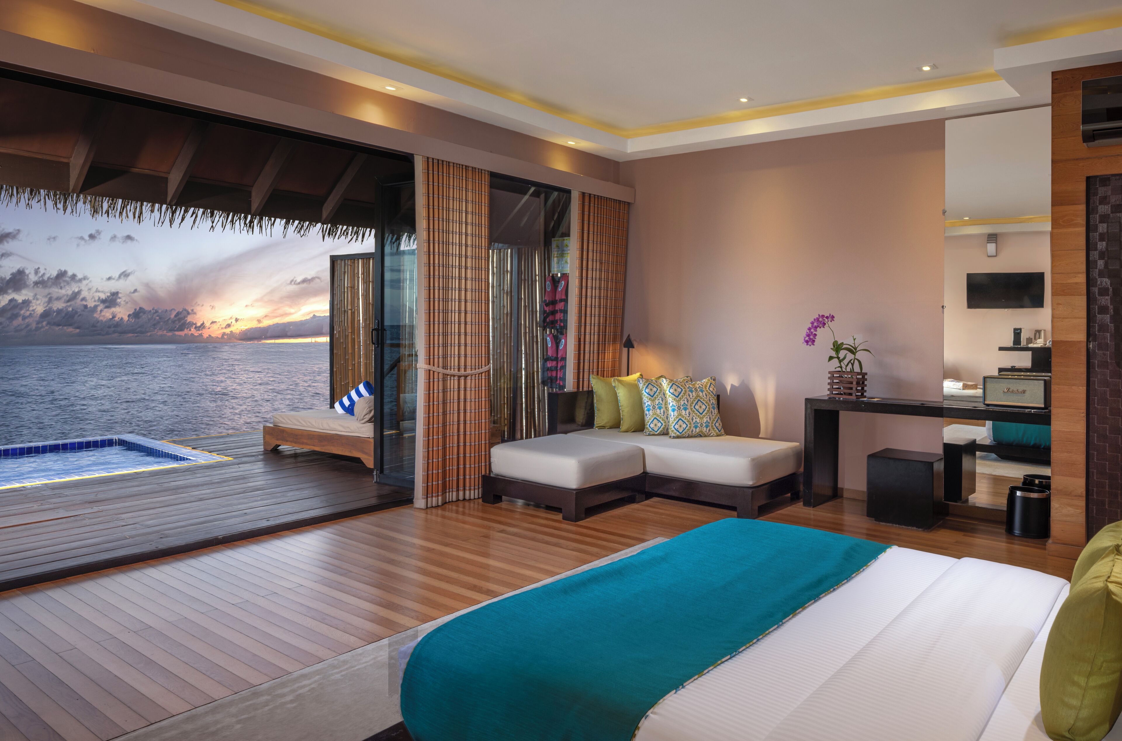 A modern bedroom with a large bed, a small sofa, a desk, and a view of the ocean.