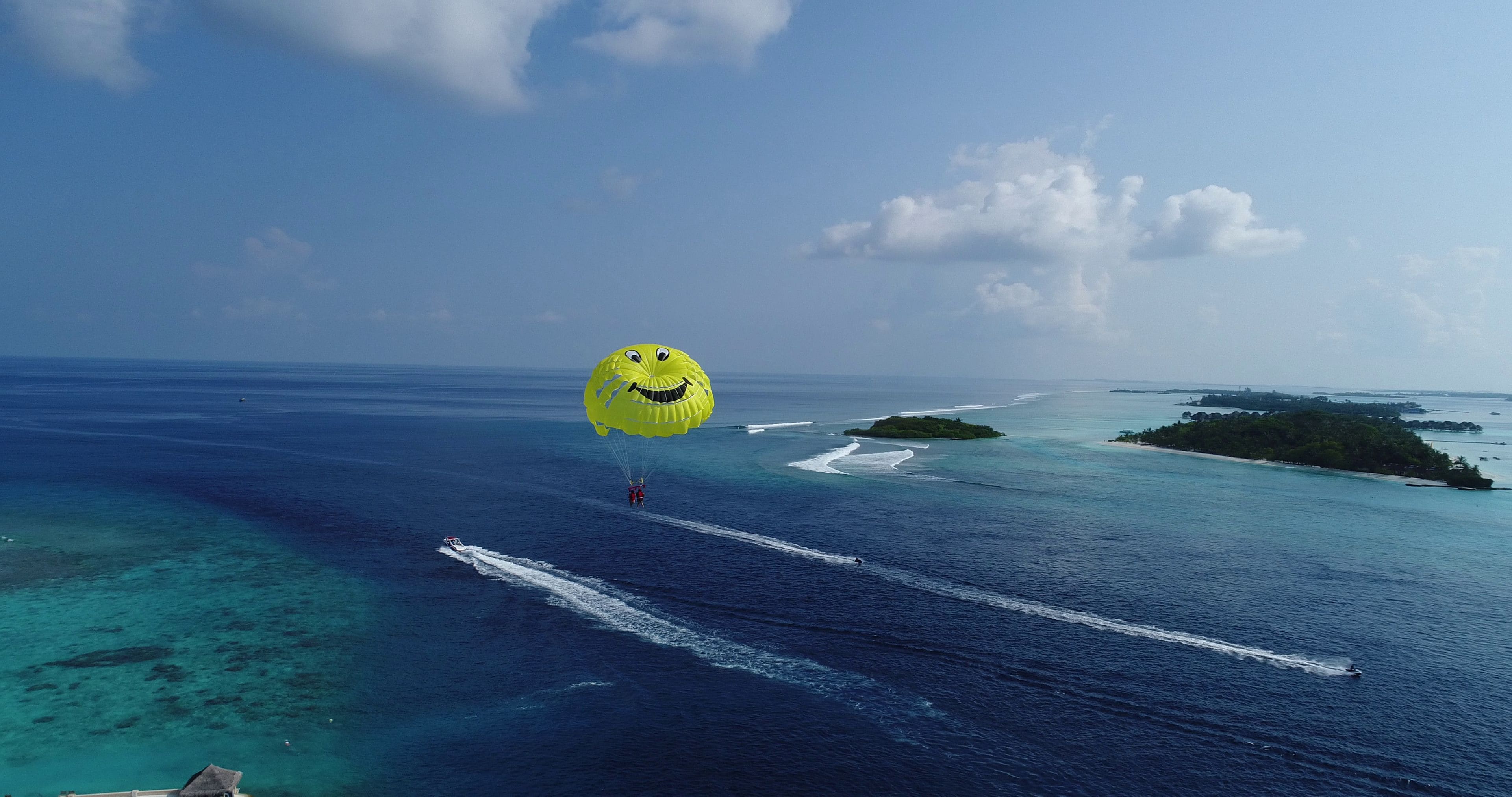 A parasailing activity over a clear blue sea with distant islands and a boat creating wake patterns.