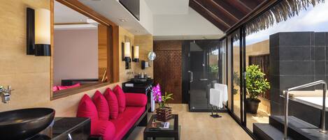 A modern bathroom with a large sink, a red sofa, a mirror, and a potted plant.