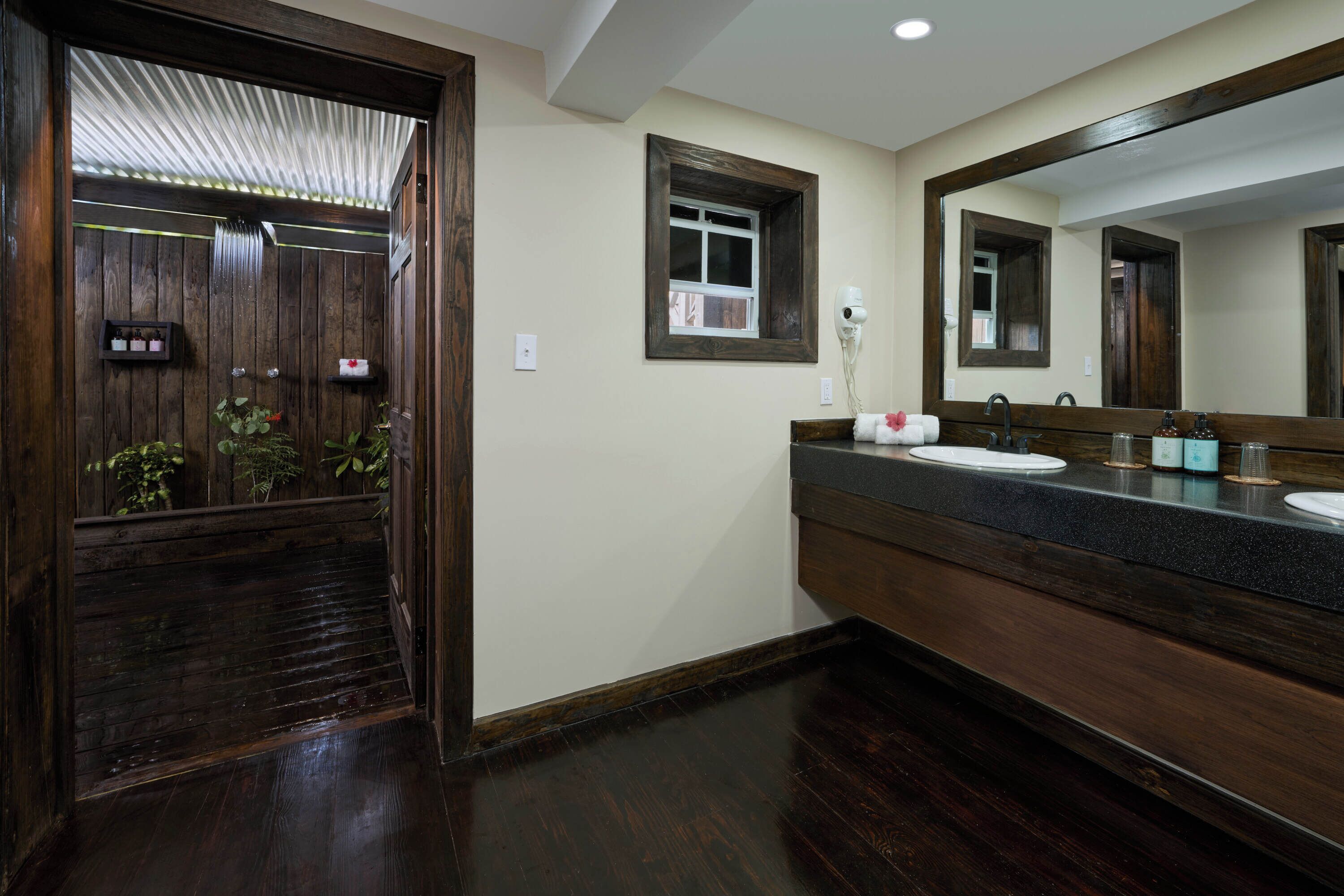 Un baño con suelo de madera, un espejo grande, un lavamanos y una ventana.