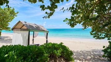Uma praia com um pequeno gazebo, águas azul-claras e vegetação exuberante.