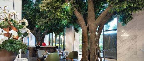 Un espacio interior con un árbol artificial grande, zonas de estar y un suelo de mármol.
