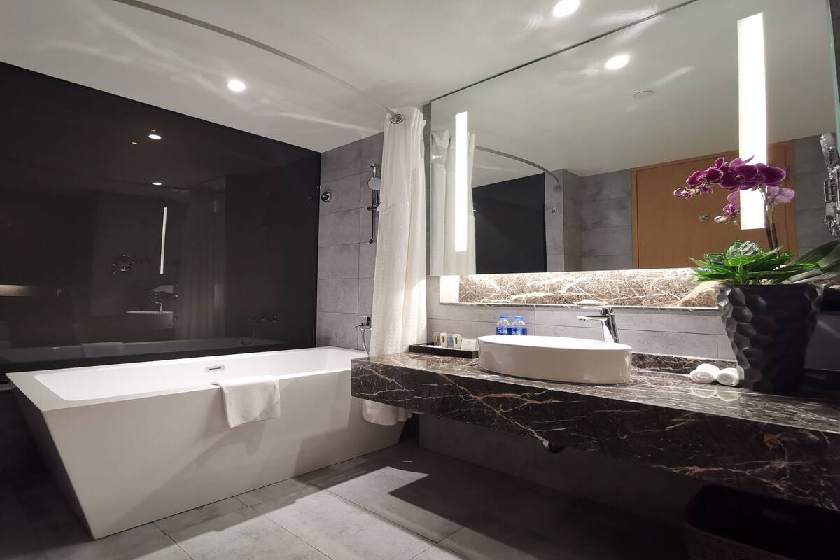 A modern bathroom with a large bathtub, a sink with a marble countertop, and a shower area.