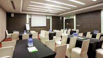 Un salón de conferencias con mesas y sillas, equipado con botellas de agua y una pantalla de proyector.
