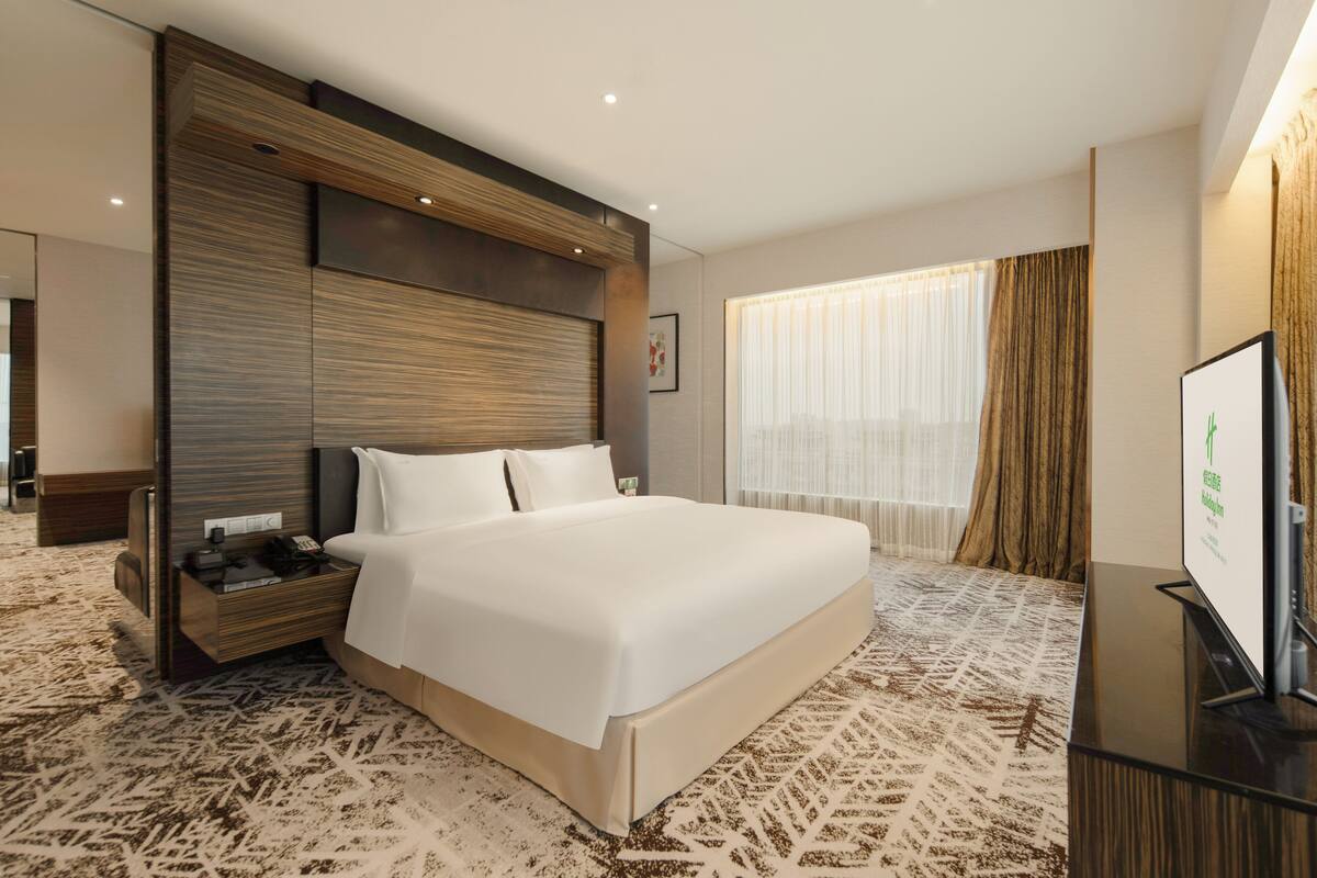 A hotel room with a large bed, a wooden headboard, a flat-screen TV, and a patterned carpet.
