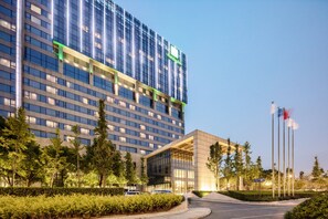 A modern hotel with a glass facade, a prominent sign, and a landscaped entrance area.