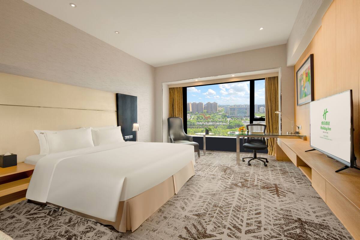 A hotel room with a large bed, a desk with a computer, a chair, and a TV.