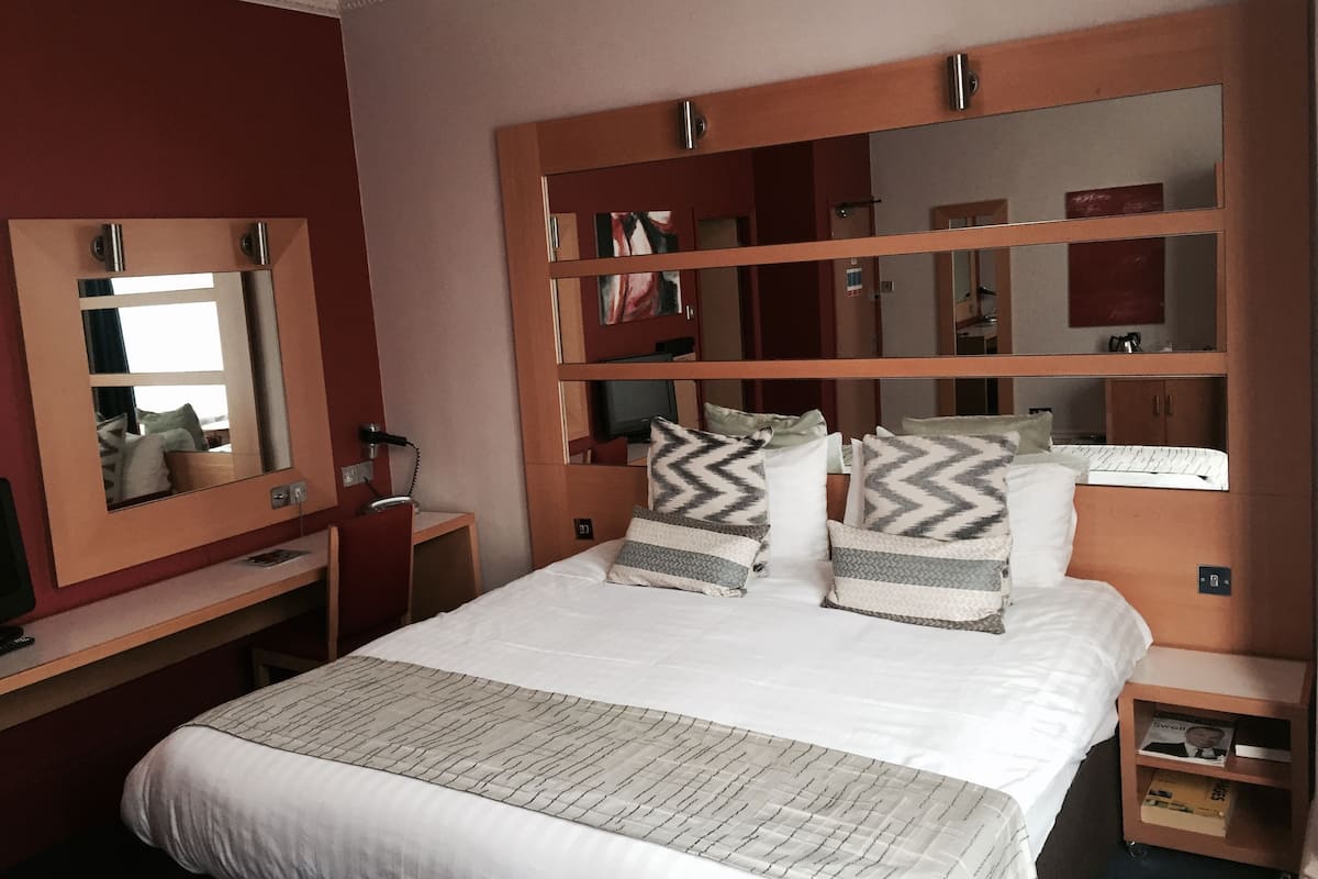 Een hotelkamer met een groot bed, een bureau, een stoel, een spiegel en een garderobe.